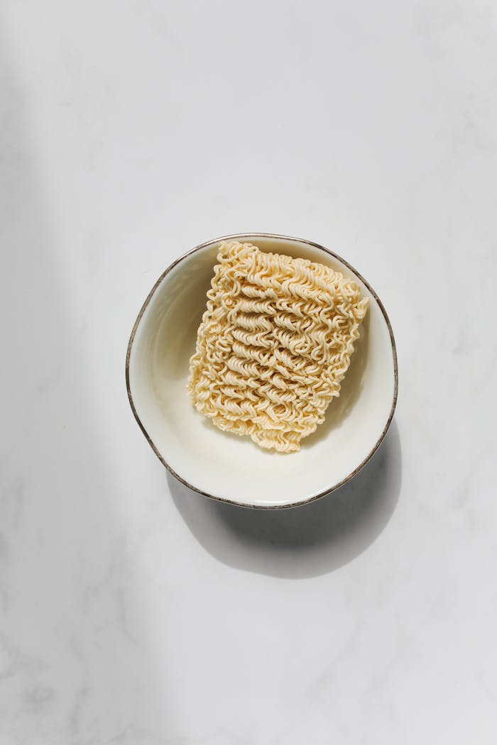 Simple flat lay of uncooked ramen noodles in a bowl on a white surface.