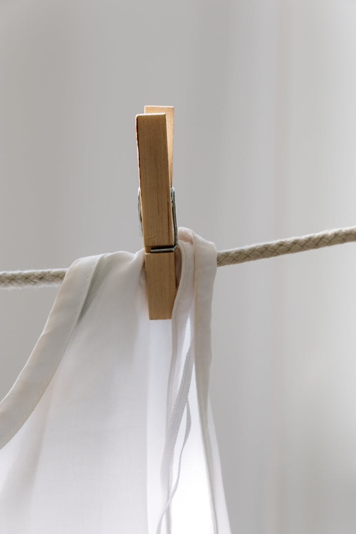 Minimalist photo of a wooden clothespin holding a white fabric on a rope, indoors.